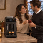 Symbolbild: Elegantes Paar in der Küche, die Frau reicht dem Mann einen Espresso in einer roten Tasse, daneben der Kaffeevollautomat